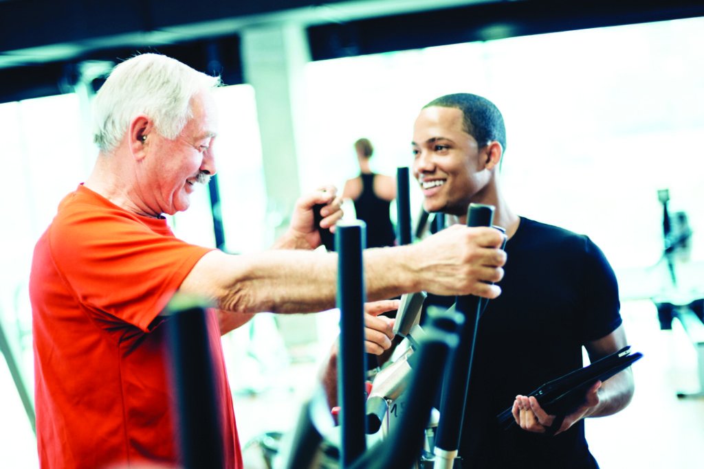Physiotherapist or Personal trainer helping senior man using Elliptical Trainers